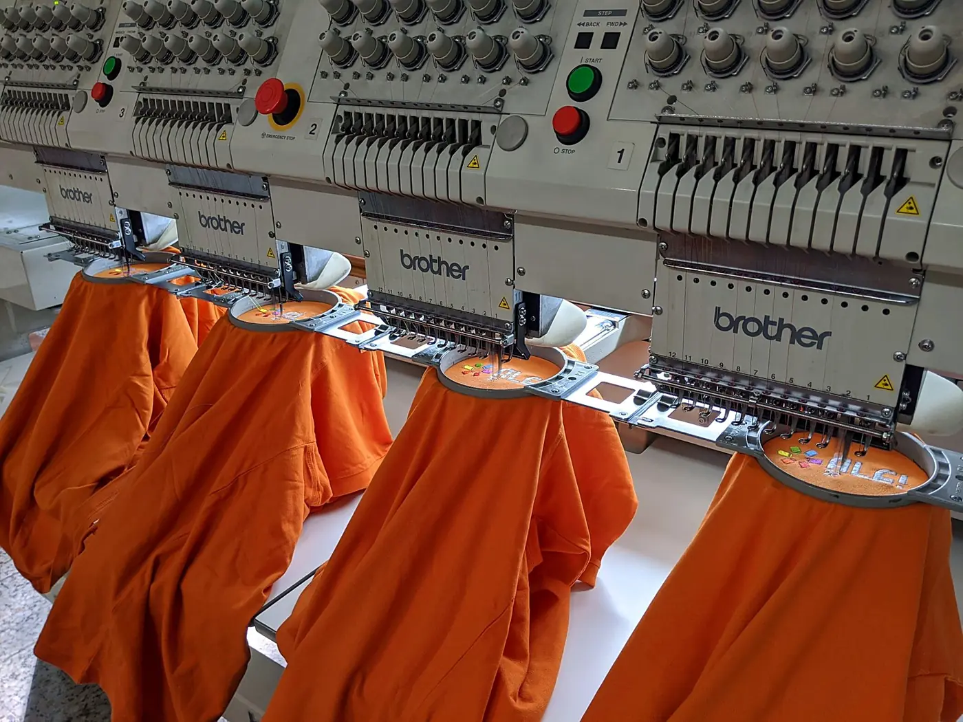 Cuatro polos naranjas bordándose a la vez en una máquina Brother de cuatro cabezales